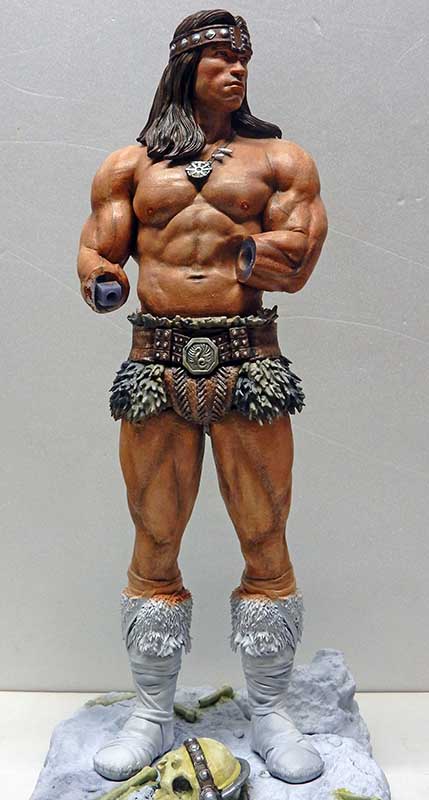 Figurine peinte de Conan musclé en pagne sur socle rocheux avec crâne