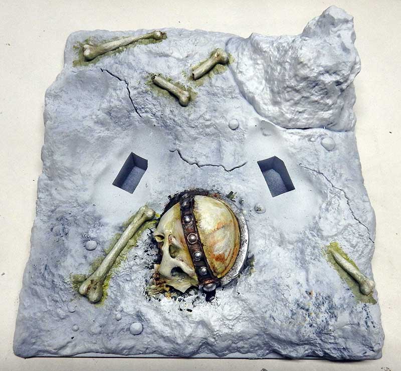 Socle de diorama rocheux avec crâne casqué et ossements peints en blanc