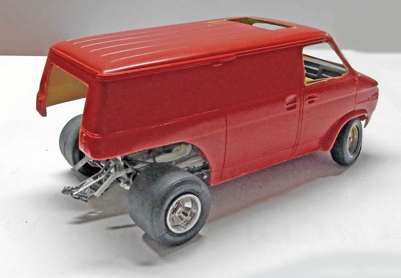 Maquette de fourgon rouge en cours de montage avec châssis et roues larges apparents