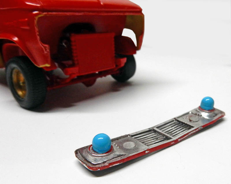 Calandre chromée avec gyrophares bleus posée devant la carrosserie rouge d'une maquette de véhicule