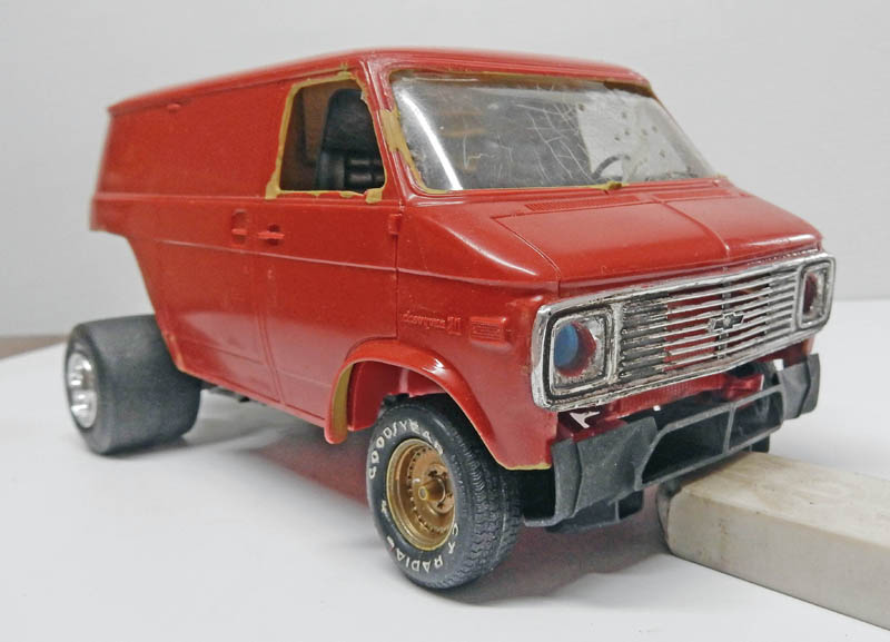 Maquette de van Chevrolet rouge en cours de montage avec masquage des vitres et calandre chromée