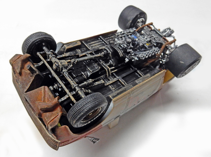 Dessous d'une maquette de voiture renversée montrant châssis et soubassement détaillés avec vieillissement et rouille