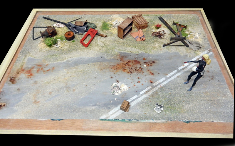 Diorama de maquette avec figurine féminine, route, débris et caisses sur sol contaminé