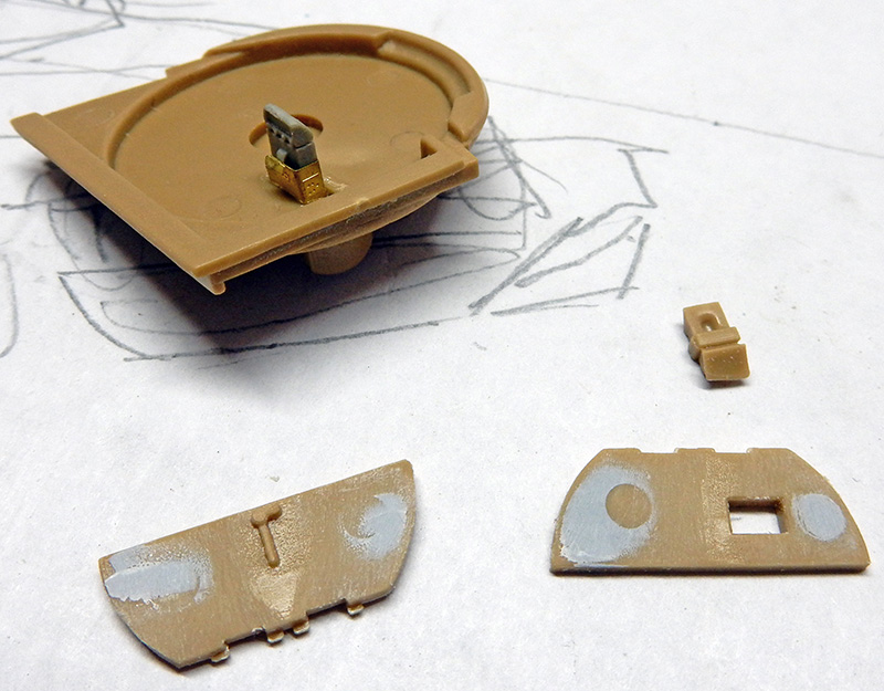 Pièces de maquette en résine beige et photodécoupe laiton posées sur un croquis crayonné