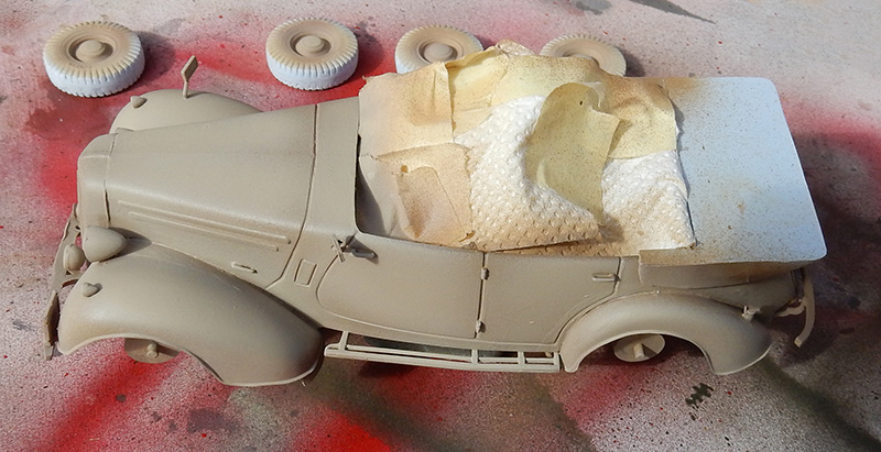 Maquette de voiture militaire décapotable peinte en sable, habitacle masqué, roues détachées posées à côté