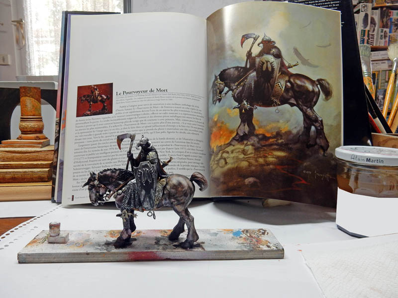 Figurine peinte d'un cavalier guerrier à la hache devant le livre illustré du Death Dealer de Frazetta