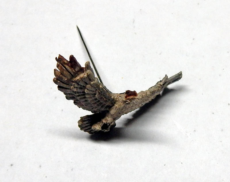 Petite figurine d'oiseau aux ailes déployées montée sur tige, posée sur fond blanc