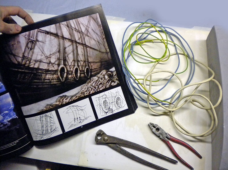 Livre de concept art ouvert, fils électriques colorés et pinces sur l'établi de maquettiste