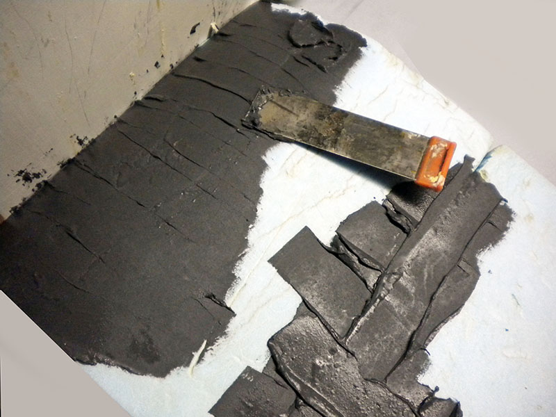 Application d'enduit gris au couteau à enduire sur maquette de décor en relief