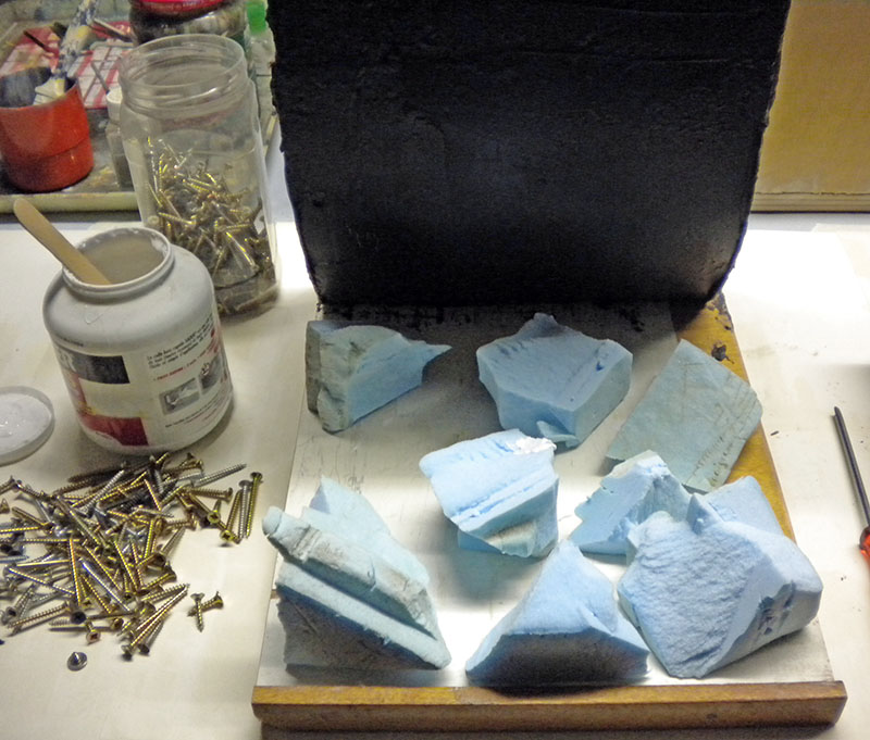 Blocs de mousse bleue découpés sur un socle en bois, vis et pot de colle sur l'établi