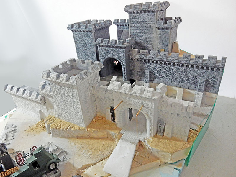 Château médiéval en construction, murailles et tours peintes en gris, terrain sablonneux non terminé