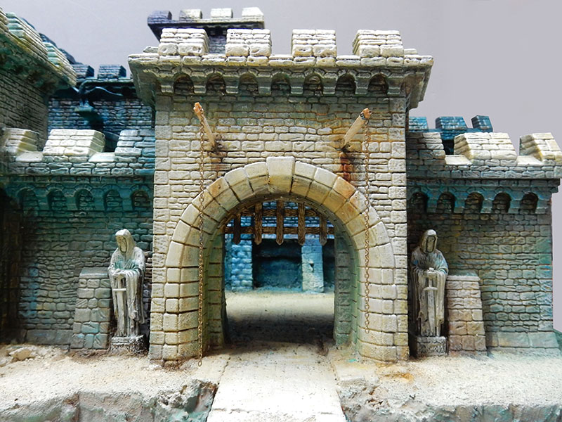 Porte fortifiée du château avec herse, chaînes et statues de gardiens en pierre