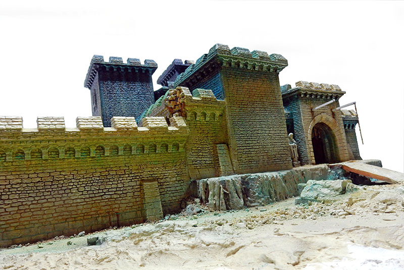 Remparts crénelés et porte fortifiée du château peints, posés sur un sol sableux clair