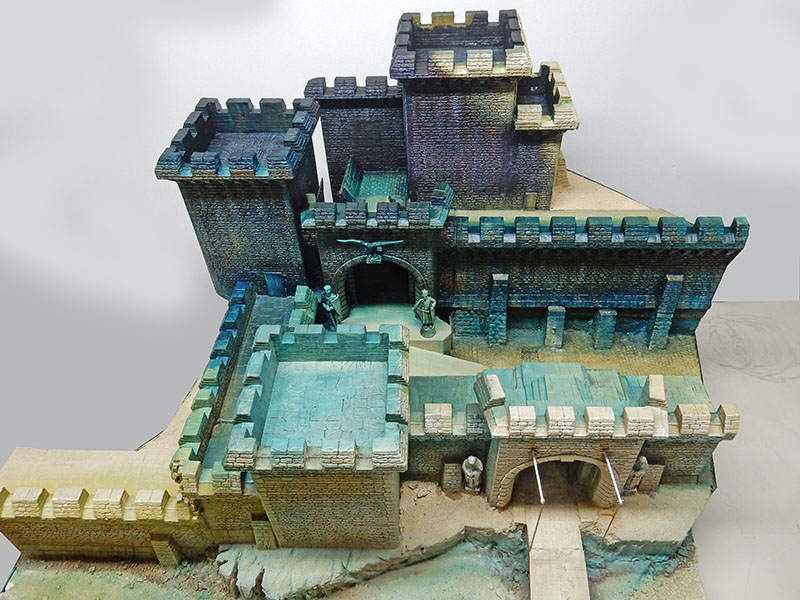 Maquette de forteresse en cours de peinture, tours crénelées et remparts teintés vert-bleu