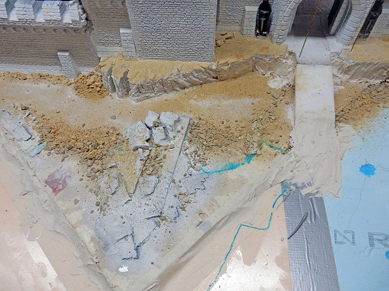 Étape de construction du décor, sol texturé et gravats au pied des ruines en briques