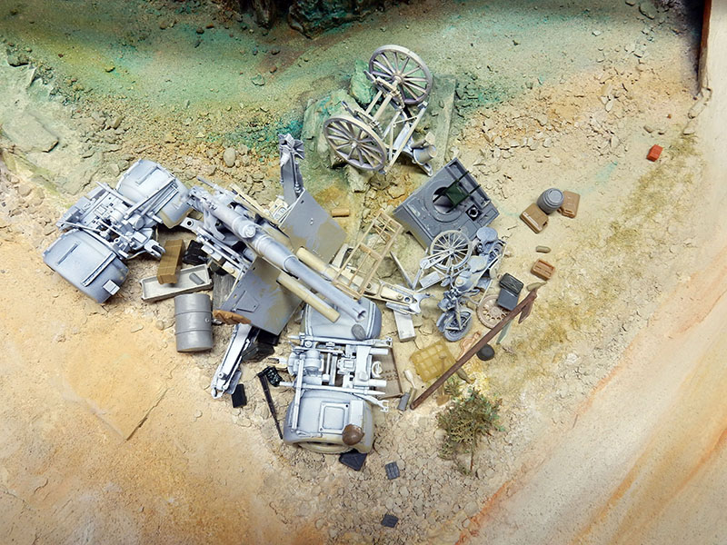 Épaves et matériel militaire non peints disposés sur le décor du diorama en préparation