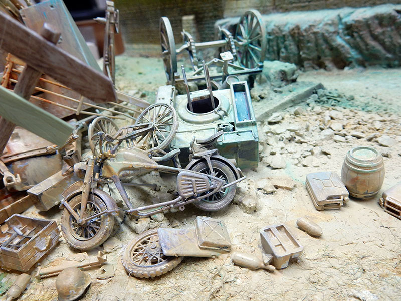 Diorama en apprêt : side-car, motos, bidons et débris devant un mur ruiné