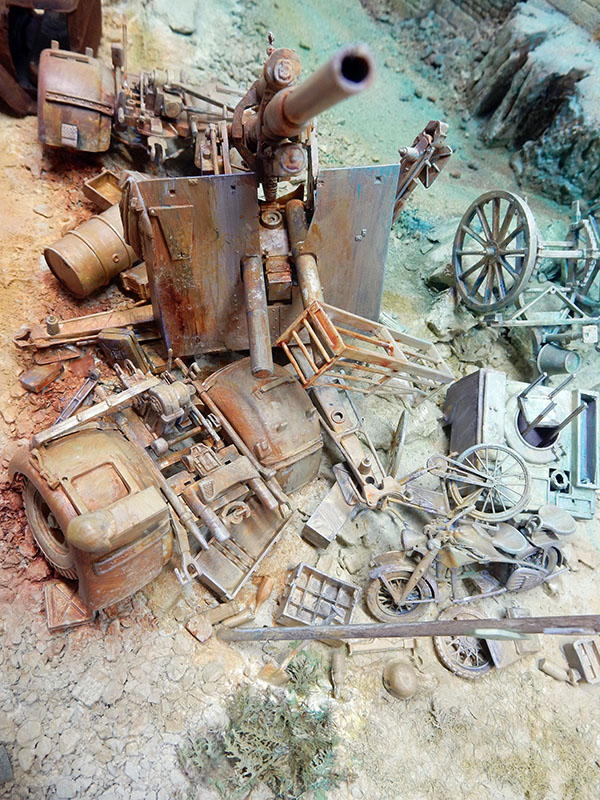 Diorama d'un amoncellement de véhicules et canon rouillés, moto et débris de guerre