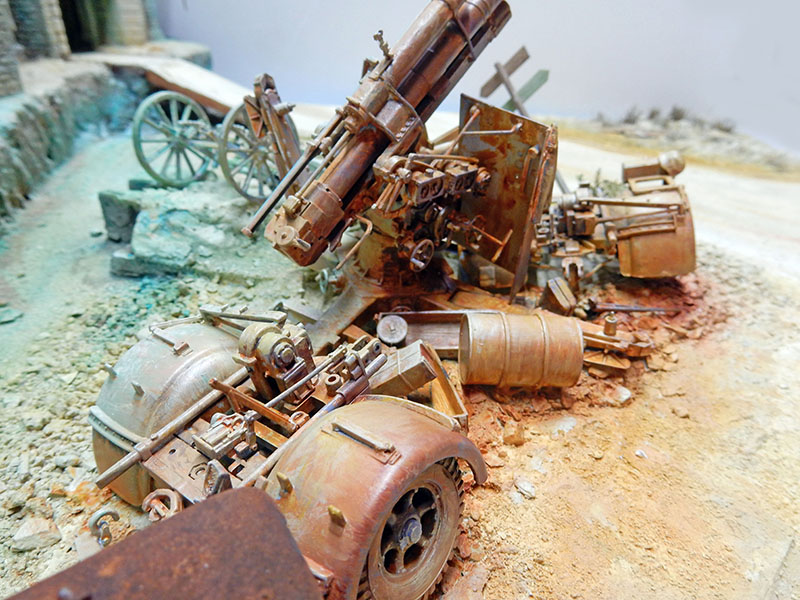 Diorama de canons antiaériens rouillés abandonnés parmi gravats et ruines, sol sablonneux