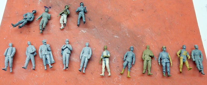 Alignement de figurines de soldats en cours de peinture, sous-couches grises et vertes