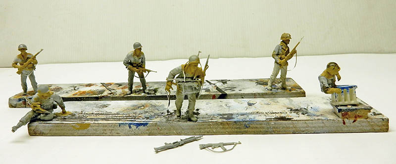 Six figurines de soldats en cours de peinture, apprêt gris, fixées sur planchettes d'atelier