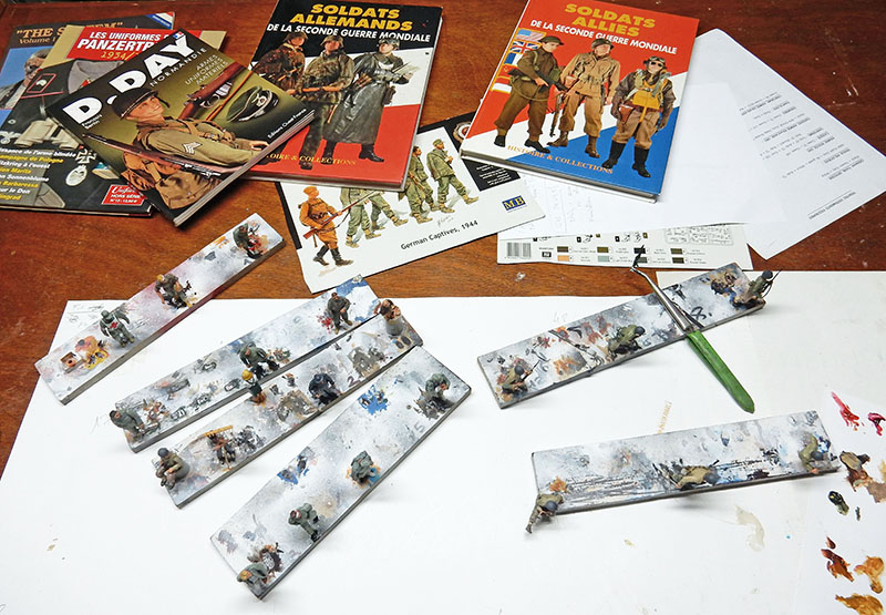 Figurines en cours de peinture sur réglettes, entourées d'ouvrages de documentation militaire
