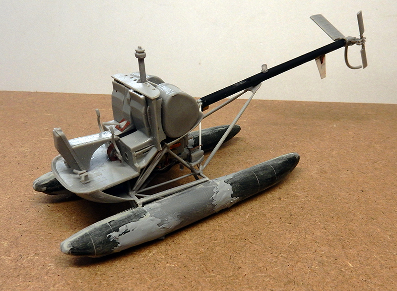 Maquette d'hélicoptère gris à flotteurs vieillis, sans rotor, posé sur fond ocre