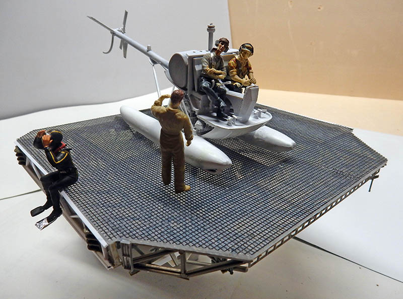 Maquette d'hélicoptère à flotteurs avec figurines de l'équipage sur une plateforme grillagée