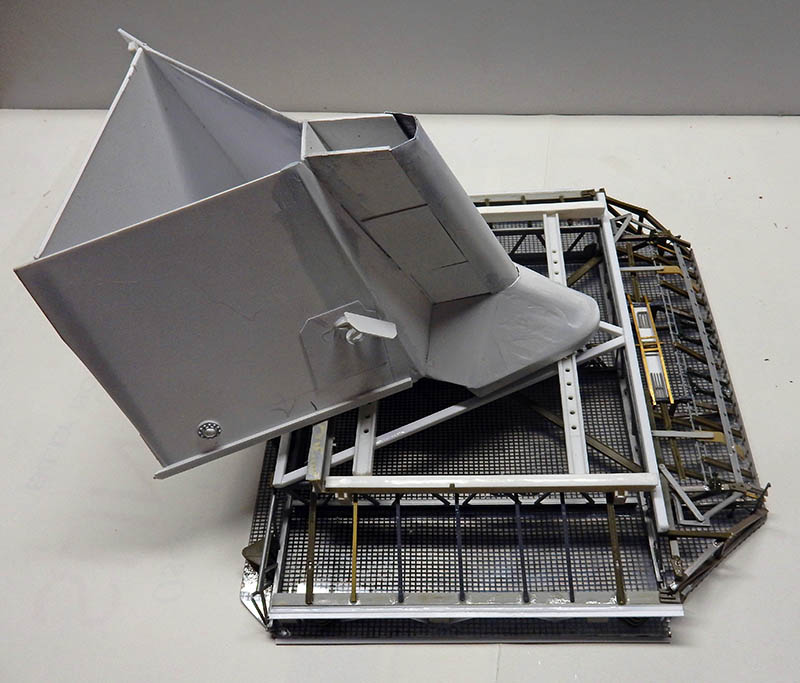 Maquette de proue grise en construction posée sur une structure métallique ajourée blanche et laiton