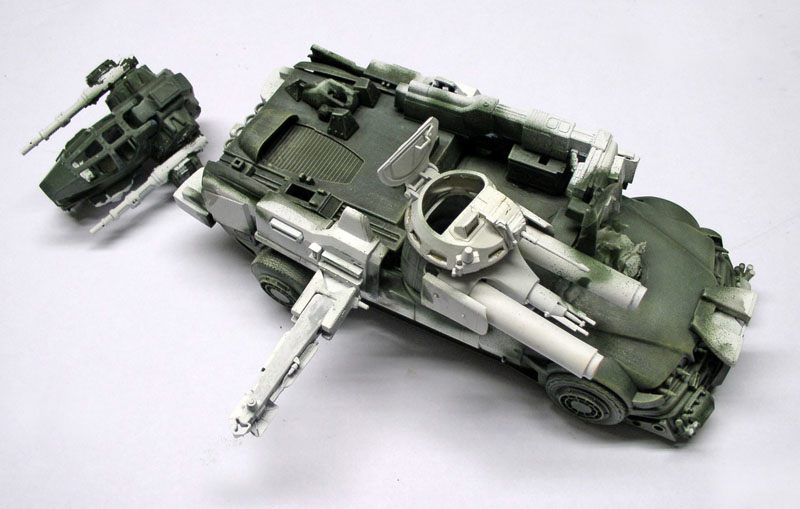 Maquette de véhicule blindé sci-fi en cours de peinture camouflage vert, tourelle séparée posée à côté