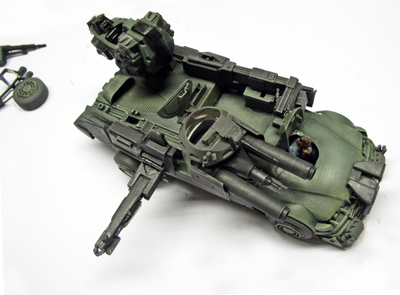 Maquette de véhicule militaire futuriste vert kaki armé, avec pièces détachées sur fond blanc