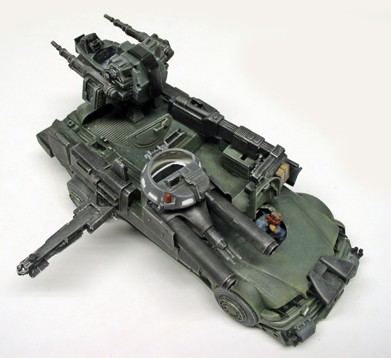 Maquette de véhicule blindé militaire vert futuriste avec tourelles armées et figurine pilotée, fond blanc