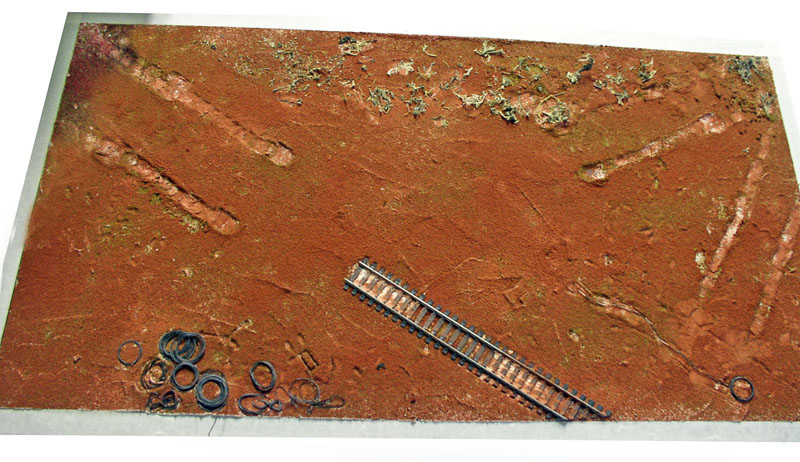 Maquette de sol martien rougeâtre avec rail miniature et anneaux métalliques posés sur le diorama