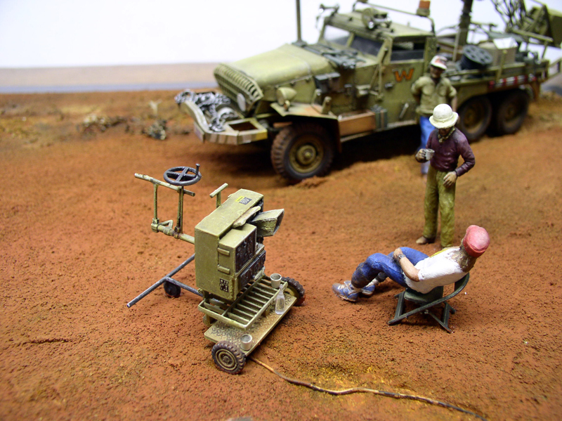 Diorama de maquettisme avec camion militaire kaki, figurines et caméra sur sol désertique rouge