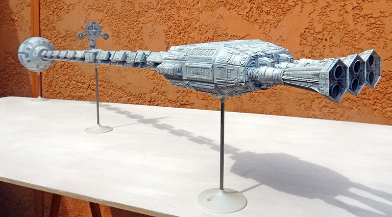 Maquette du vaisseau spatial Discovery sur supports, posée devant un mur orange