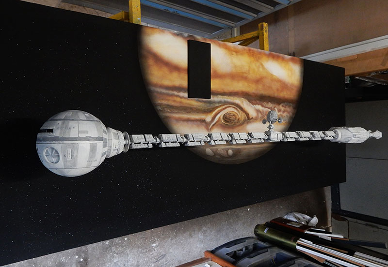 Maquette du vaisseau spatial Discovery devant Jupiter et le monolithe noir sur diorama