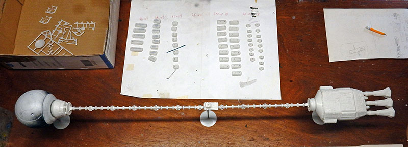 Maquette du vaisseau Discovery en cours d'assemblage avec pièces grises alignées et plans sur l'établi