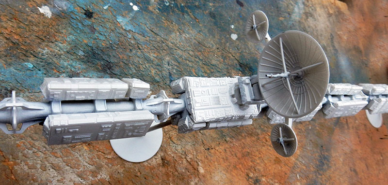 Maquette grise du vaisseau spatial Discovery avec antennes paraboliques et modules, sur fond rocheux