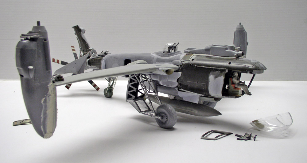 Maquette d'avion militaire gris en cours d'assemblage avec verrière et pièces détachées posées à côté