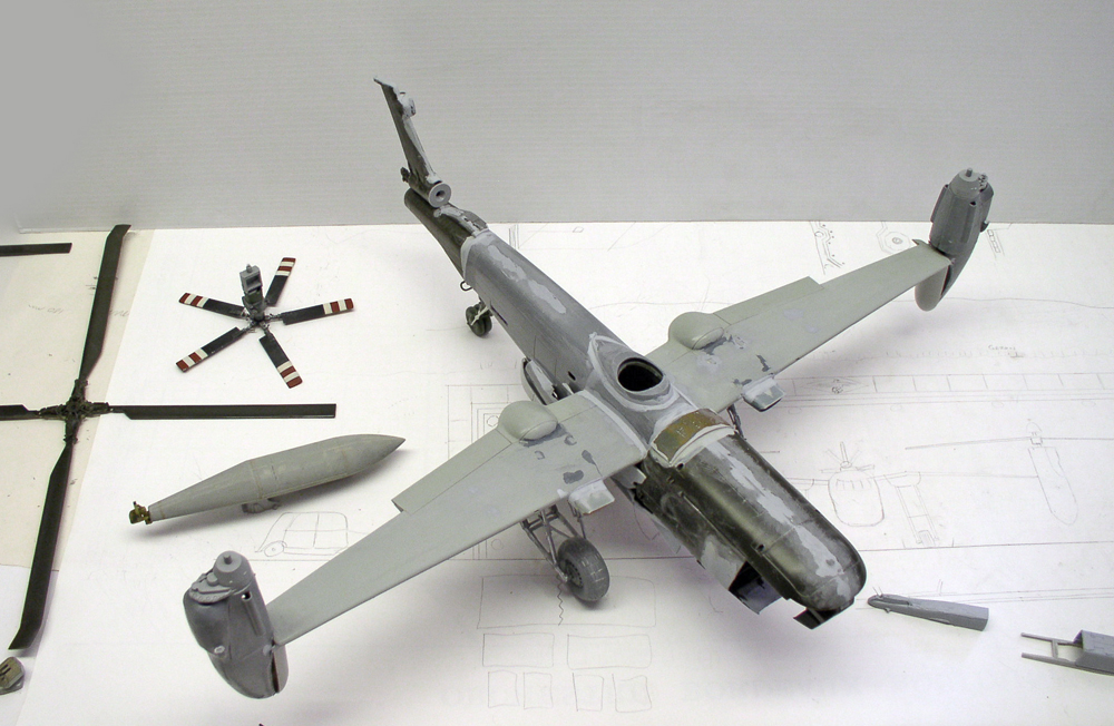 Maquette d'hélicoptère gris en cours de montage avec rotor démonté posé sur des plans