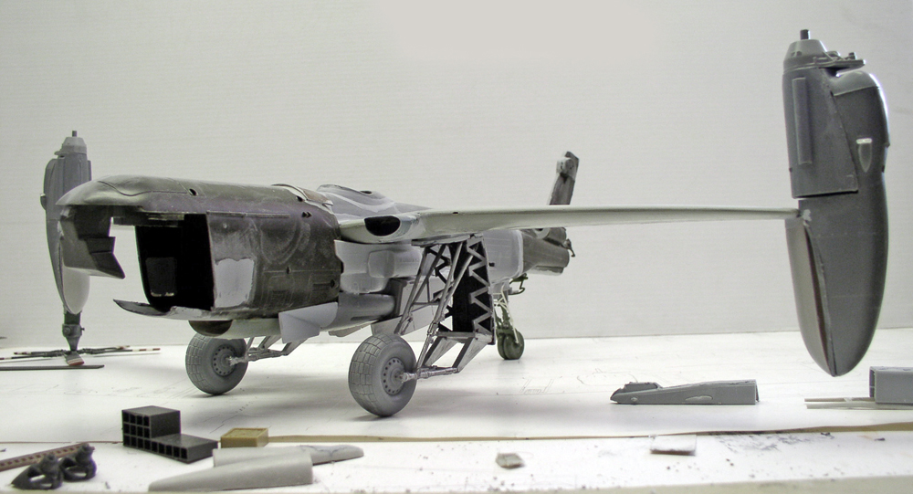 Maquette d'avion bimoteur en cours d'assemblage avec train d'atterrissage et pièces grises éparses sur l'établi