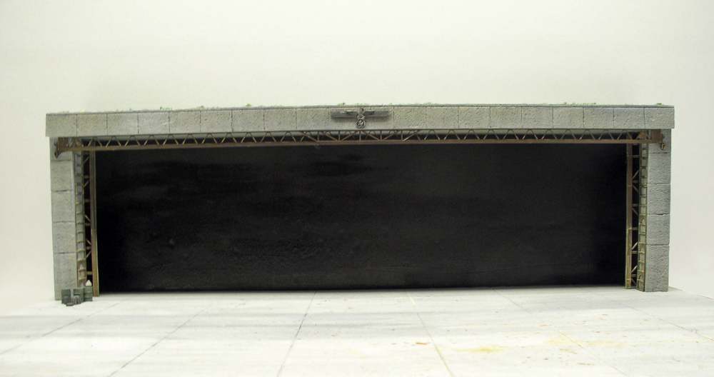 Maquette d'un grand bunker en béton gris avec large ouverture sombre et charpente métallique