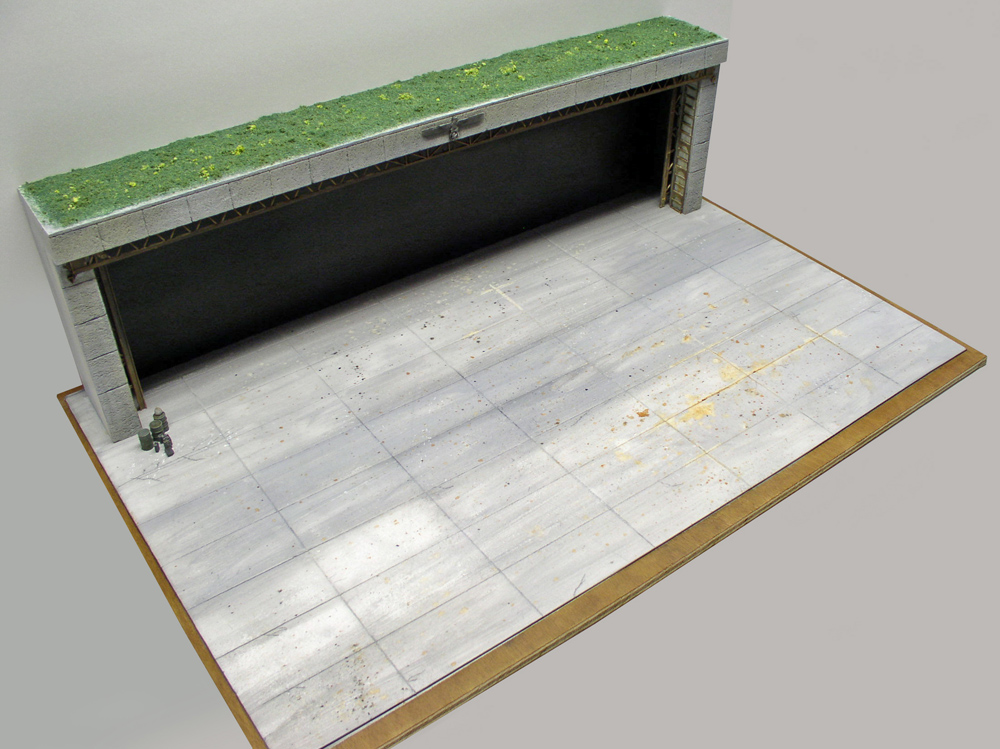 Maquette de bunker souterrain avec entrée bétonnée, toit végétalisé et large dalle pavée