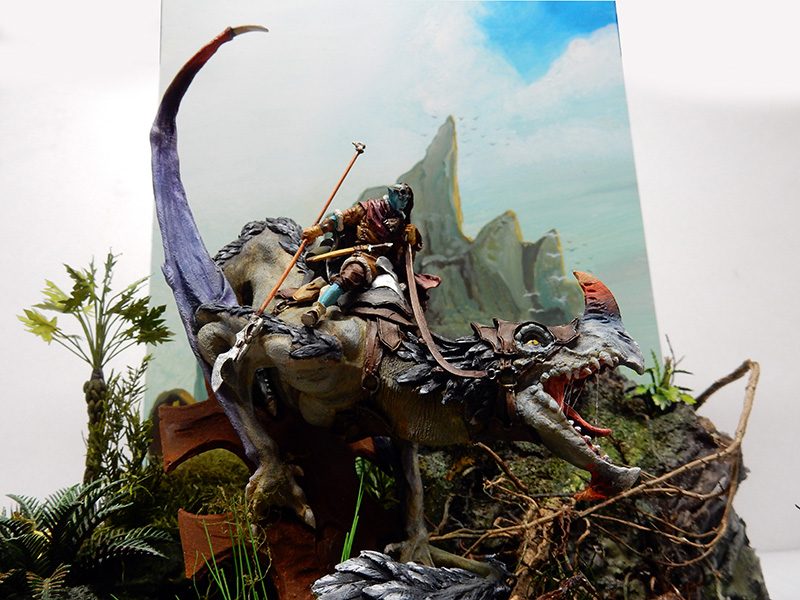 Diorama de maquette représentant un dragon ailé gueule ouverte chevauché par un guerrier dans un décor montagneux