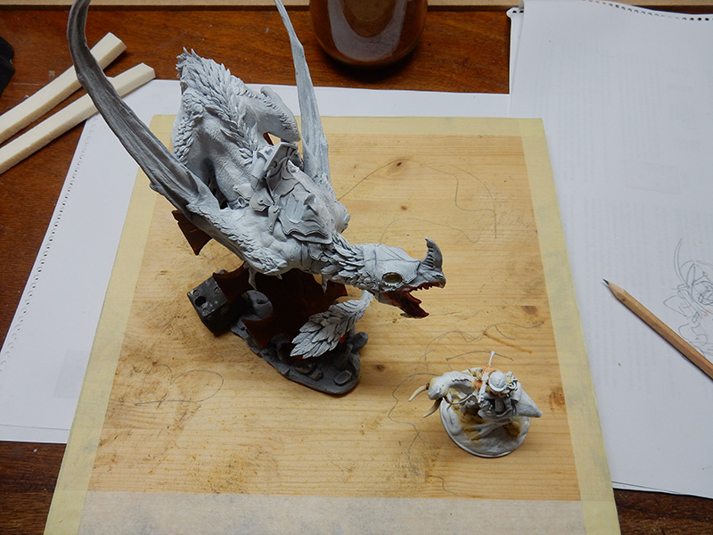 Maquette de dragon gris non peinte ailes déployées à côté d'une figurine sur établi