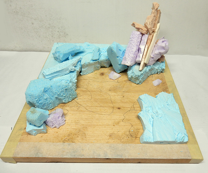 Maquette de diorama en construction avec rochers en mousse bleue et structure en bois sur socle