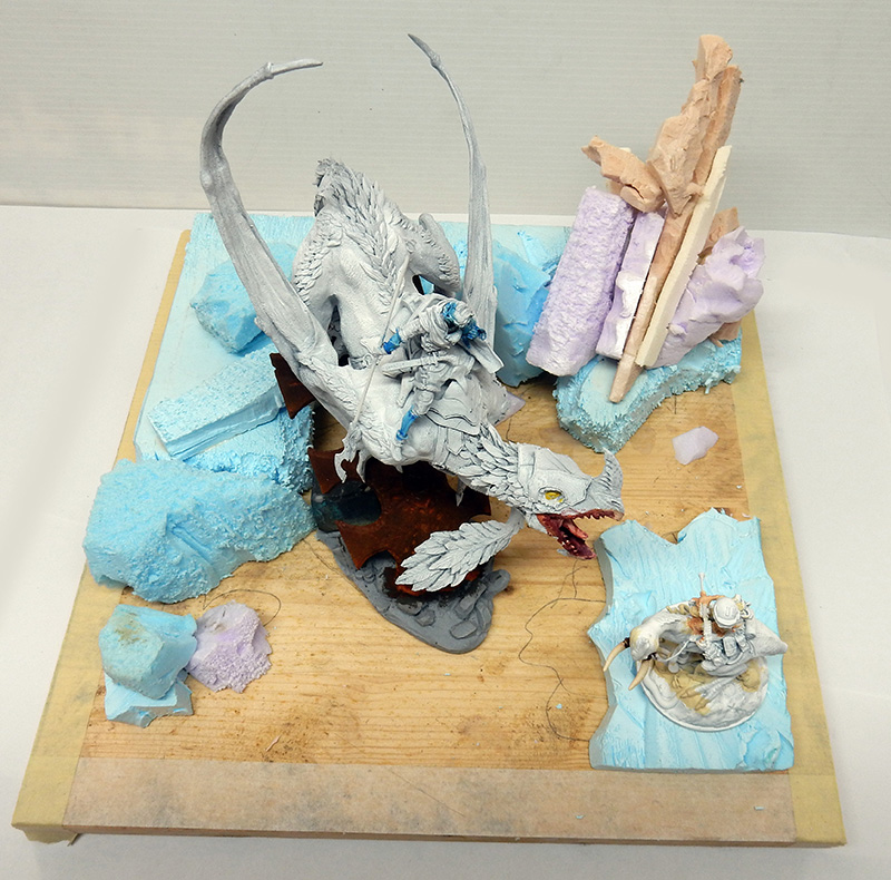 Diorama en cours de maquette d'un dragon blanc chevauché, entouré de blocs de polystyrène bleu