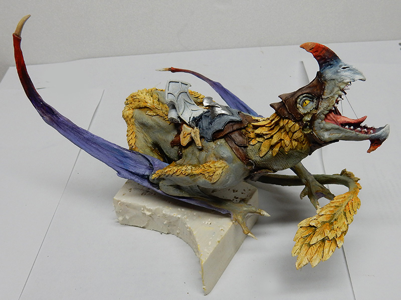 Figurine de dragon peinte gueule ouverte, ailes violettes et crinière jaune, sur socle