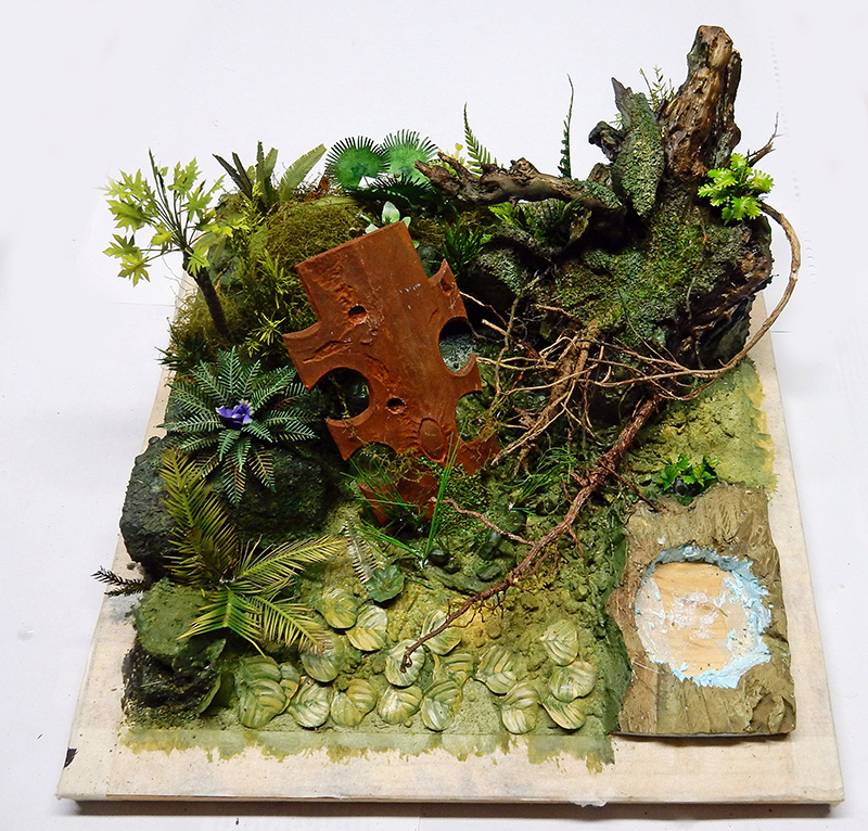 Diorama de maquette représentant une jungle luxuriante avec rochers moussus, plantes tropicales et petit bassin d'eau