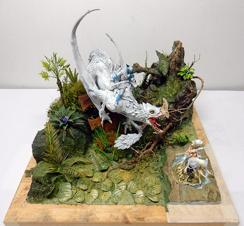 Diorama de maquettisme avec un dragon blanc chevauché par un cavalier dans une végétation luxuriante